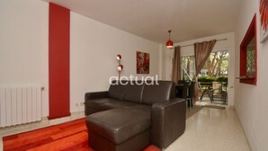 Un salon moderne avec un canapé en cuir marron, un mur d’accent rouge et une vue sur un espace patio extérieur.