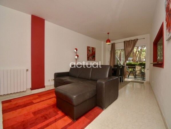 A modern living room with a brown leather sofa, a red accent wall, and a view of an outdoor patio area.