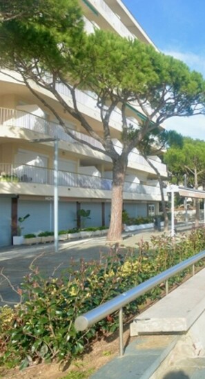 A multi-story building with balconies, a tree in the foreground, and a metal railing along the sidewalk. - Modern apartment in Platja d'Aro with air conditioning and parking (Platja d'Aro)