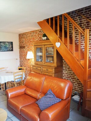 A living room with a brown leather sofa, a wooden staircase, a brick wall, and a cabinet with glass doors. - Les Buis  (Sainghin-en-Weppes)