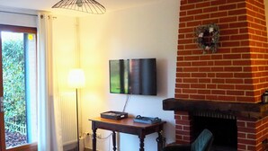 Una sala de estar con chimenea, televisor montado en la pared, una mesa con sillas y una ventana con cortinas.