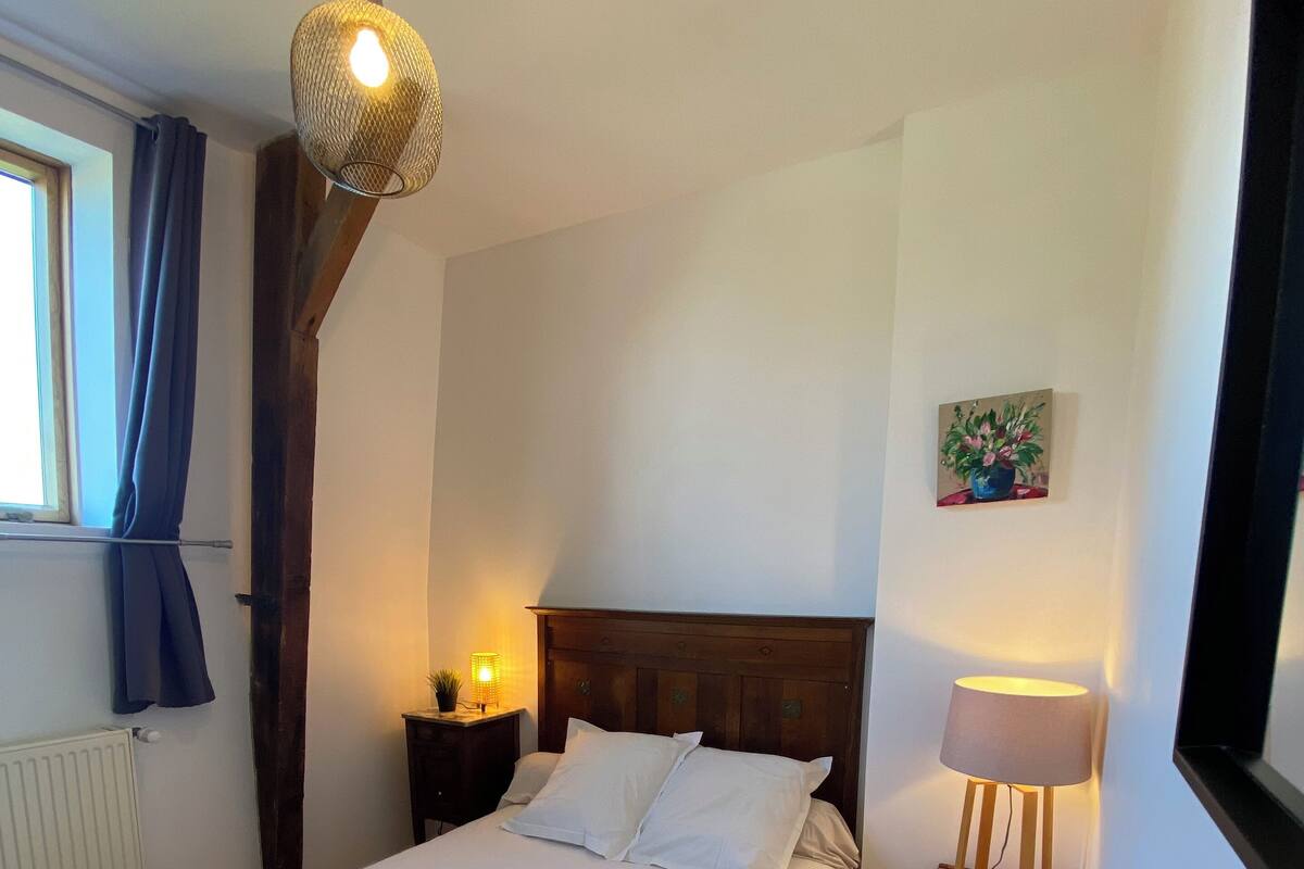 A neatly made bed with white linens, a wooden headboard, a bedside lamp, and a hanging light fixture.
