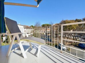 Un balcon avec une chaise blanche, une balustrade et une vue sur un parking et des bâtiments en arrière-plan.