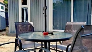 Un espace patio comprenant une table ronde en verre et quatre chaises, un parasol, ainsi qu’une porte-fenêtre coulissante donnant sur un porche abrité.