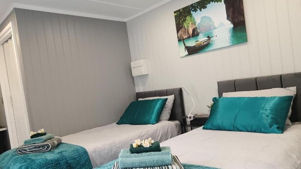 Une chambre d’hôtel avec deux lits, chacun agrémenté de draps et d’oreillers de couleur turquoise, une table de chevet avec une lampe et un tableau représentant un paysage côtier accroché au mur.