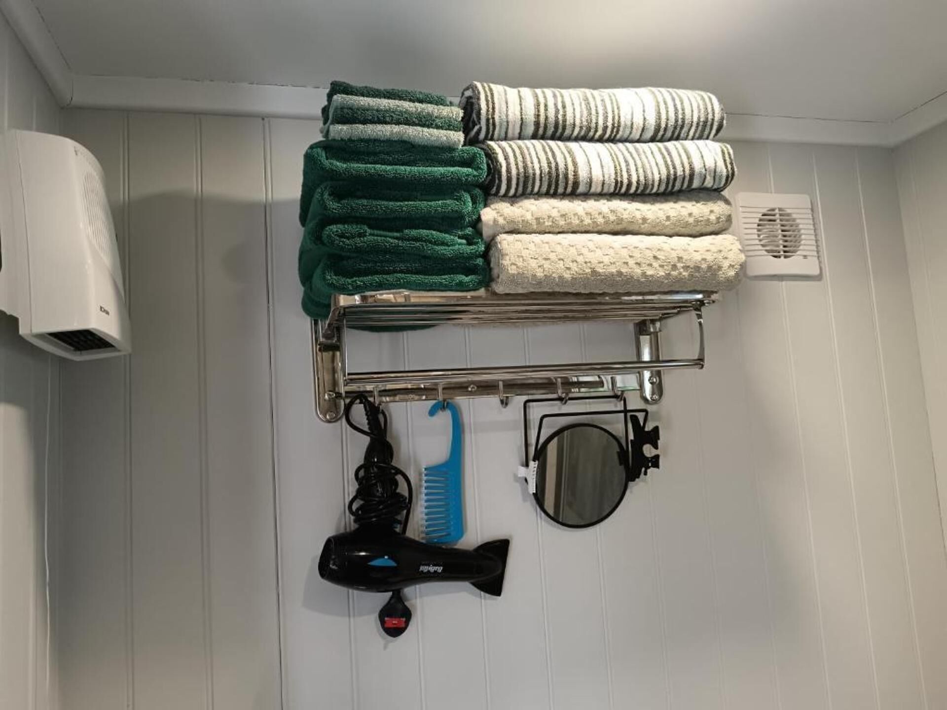 Casa de banho com porta-toalhas com toalhas dobradas, secador de cabelo, pente azul e espelho.