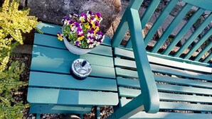 Un banc vert installé à l’extérieur, muni d’un cendrier en métal et agrémenté d’un bouquet de fleurs aux couleurs vives.
