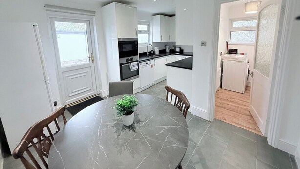 A modern kitchen with white cabinets, a black countertop, and a dining area with a marble table and chairs.