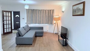A living room with a grey sectional sofa, a standing floor lamp, a television, and a door with a window.