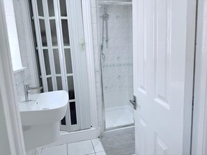 Ein Badezimmer mit einem weißen Waschbecken, einer Duschkabine aus Glas und einem gefliesten Boden.