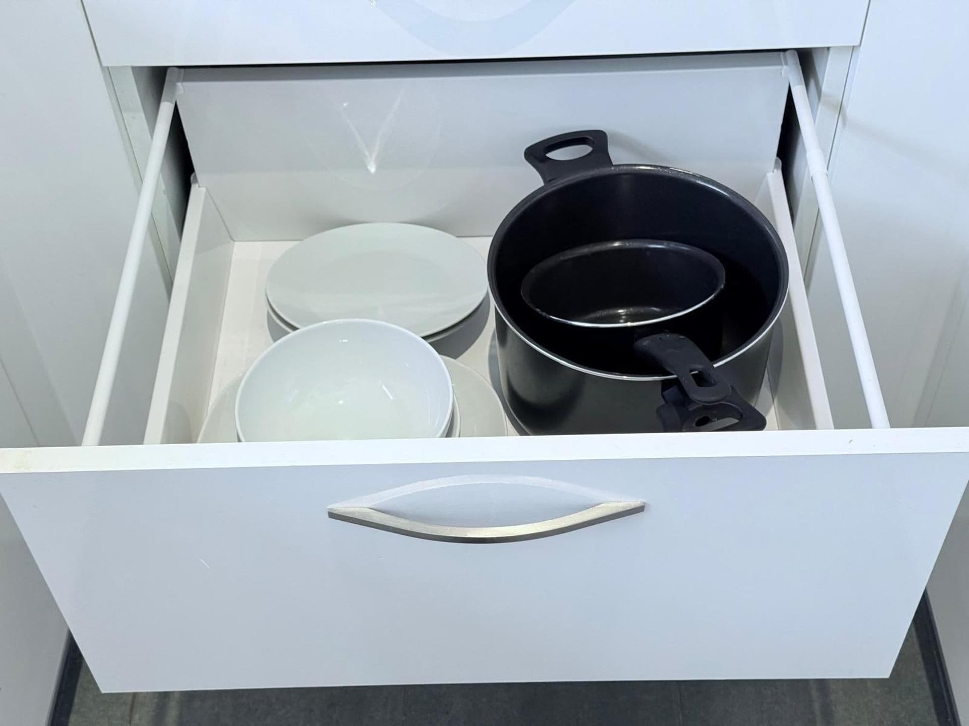 Un tiroir contenant un pot noir, deux assiettes blanches et un bol blanc.