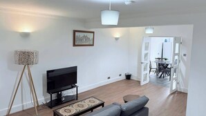 A living room with a sofa, a TV, a floor lamp, and a dining area with chairs and a table.