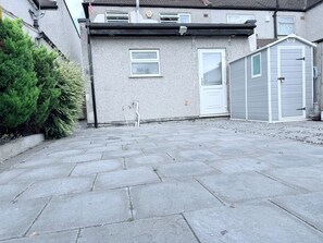 Un quartier résidentiel avec une allée pavée, une maison avec une porte blanche et un abri de jardin.