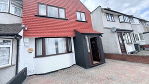 Ein zweistöckiges Haus mit rotem Dach, einer kleinen Veranda und einer Tür mit Fenster.