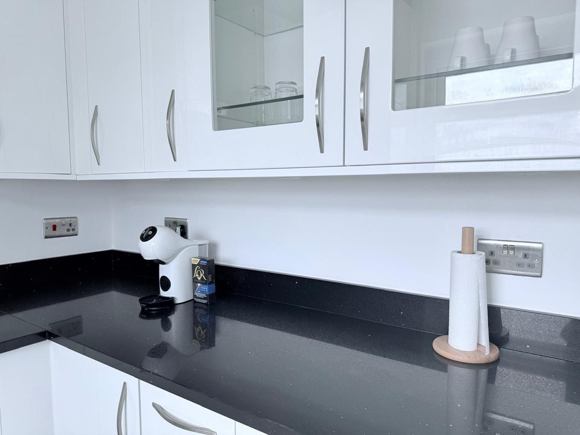 A kitchen with white cabinets, a black countertop, a coffee machine, and a paper towel holder.
