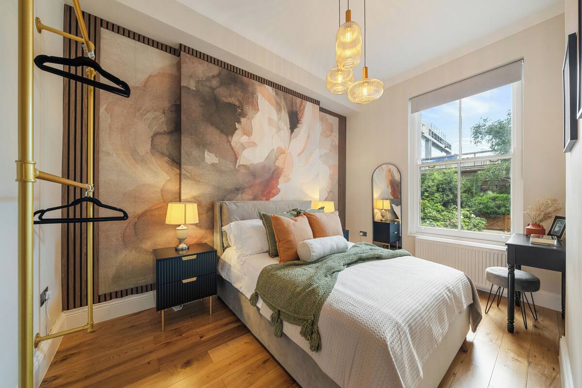 A bedroom with a large bed, a desk, a window with a view of greenery, and a wall with abstract art.