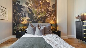 Een slaapkamer met een groot bed, twee nachtkastjes met lampen, een zwarte dressoir en een wand met een grote bloemermural.
