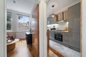 A modern kitchen with a view to the outside, wooden flooring, and a built-in oven. - Avari Apartments - Notting Hill (London)