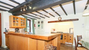 A kitchen with wooden cabinets, a central island with stools, a tiled backsplash, and a hanging light fixture.