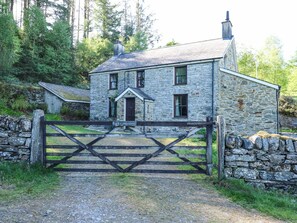 A stone house with a wooden gate, surrounded by stone walls and greenery.