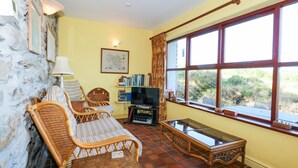 A cozy living room with wicker furniture, a television, and a large window with a view of greenery.