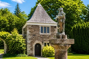 A stone building with a pointed roof, a black door, and a statue on a pedestal in front. - Lewtrenchard Manor (Okehampton)