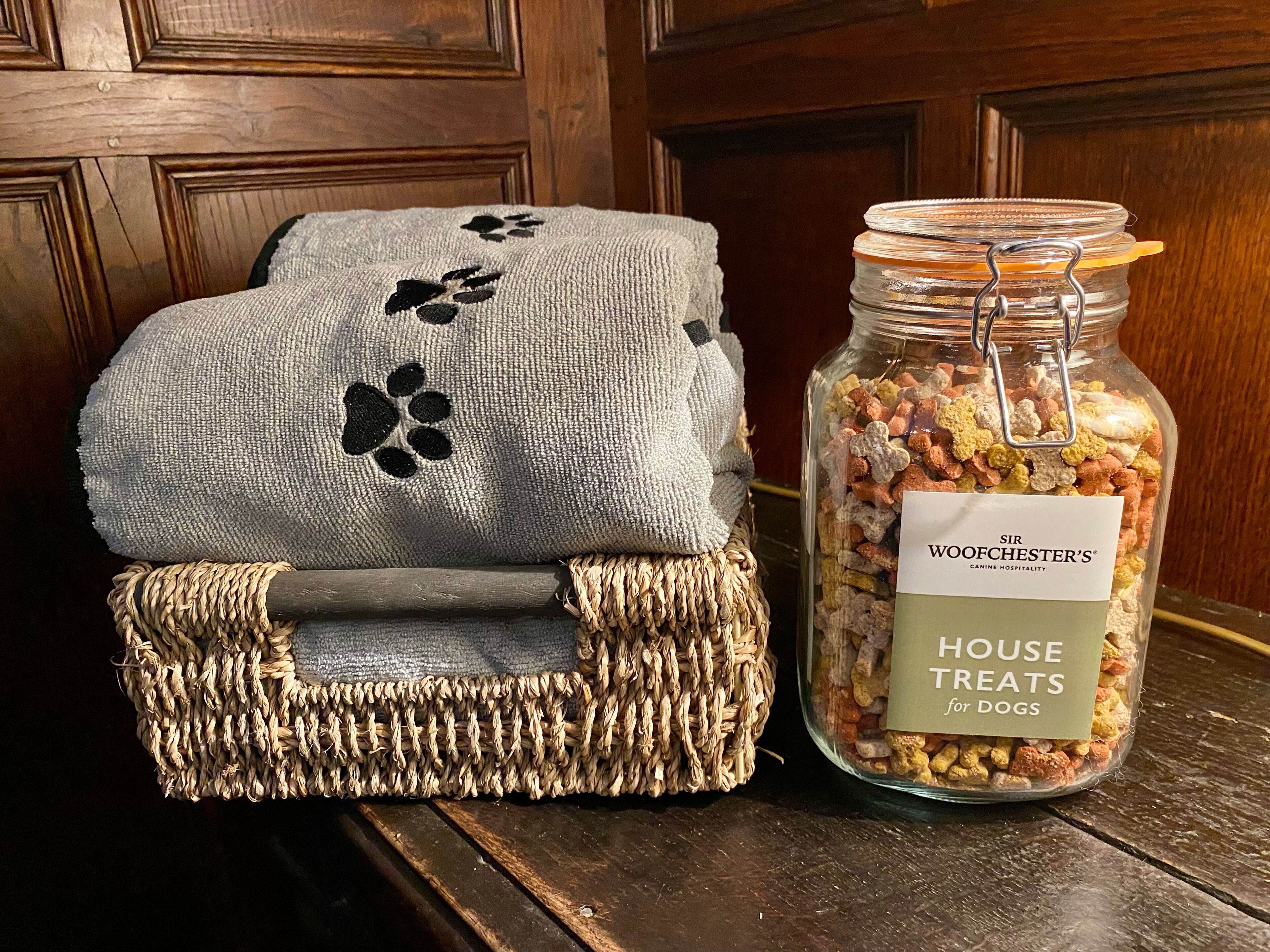 Una cesta tejida con un paño gris y un tarro etiquetado 'SIR WOODCHESTER'S HOUSE TREATS for DOGS'.