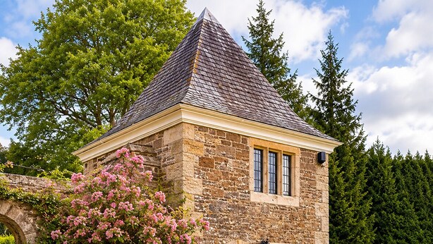 A stone building with a pitched roof, a central entrance, and a well-maintained lawn. - Lewtrenchard Manor (Okehampton)