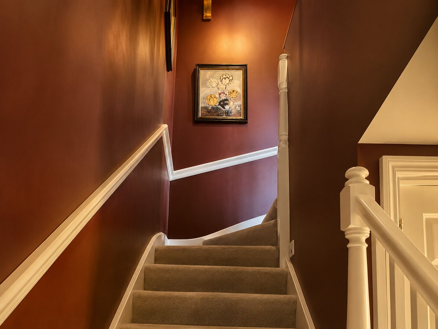 A staircase with carpeted steps, white handrails, and a wall-mounted picture frame.
