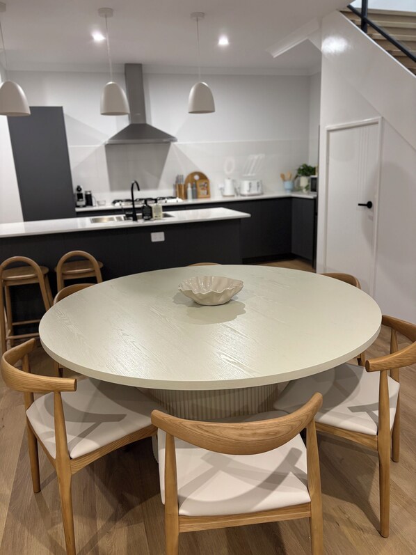 Une cuisine moderne avec une table de salle à manger ronde, des chaises en bois, des luminaires suspendus et une porte blanche.