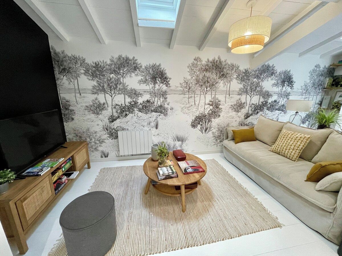 Una sala de estar con un sofá, una mesa de centro, un mueble para televisor y un mural con árboles.