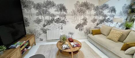 Una sala de estar con un sofá, una mesa de centro, un mueble para televisor y un mural con árboles.