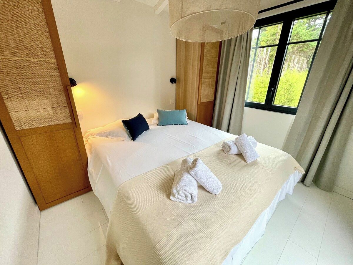 A hotel room with a bed, two towels, a nightstand, and a window with curtains.