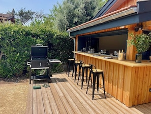 An outdoor bar area with a grill, bar stools, and a wooden deck.