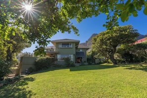 A two-story house with a well-maintained lawn, surrounded by trees and a mountain in the background. - Spacious Kinvara Villa with AC, Gym, Pool & Mountain Views (Cape Town)