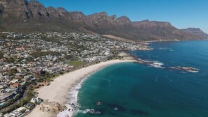 An aerial view of a coastal town with a beach, rocky mountains, and residential buildings. - Spacious Kinvara Villa with AC, Gym, Pool & Mountain Views (Cape Town)