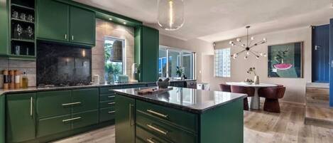 A modern kitchen with green cabinets, a marble countertop, and a central island.