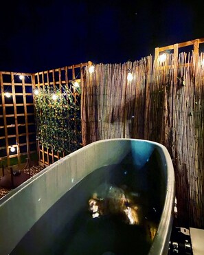 A hot tub in a garden area with a bamboo fence and wooden trellis. - Shepherd Hut Rutland Water (Oakham)