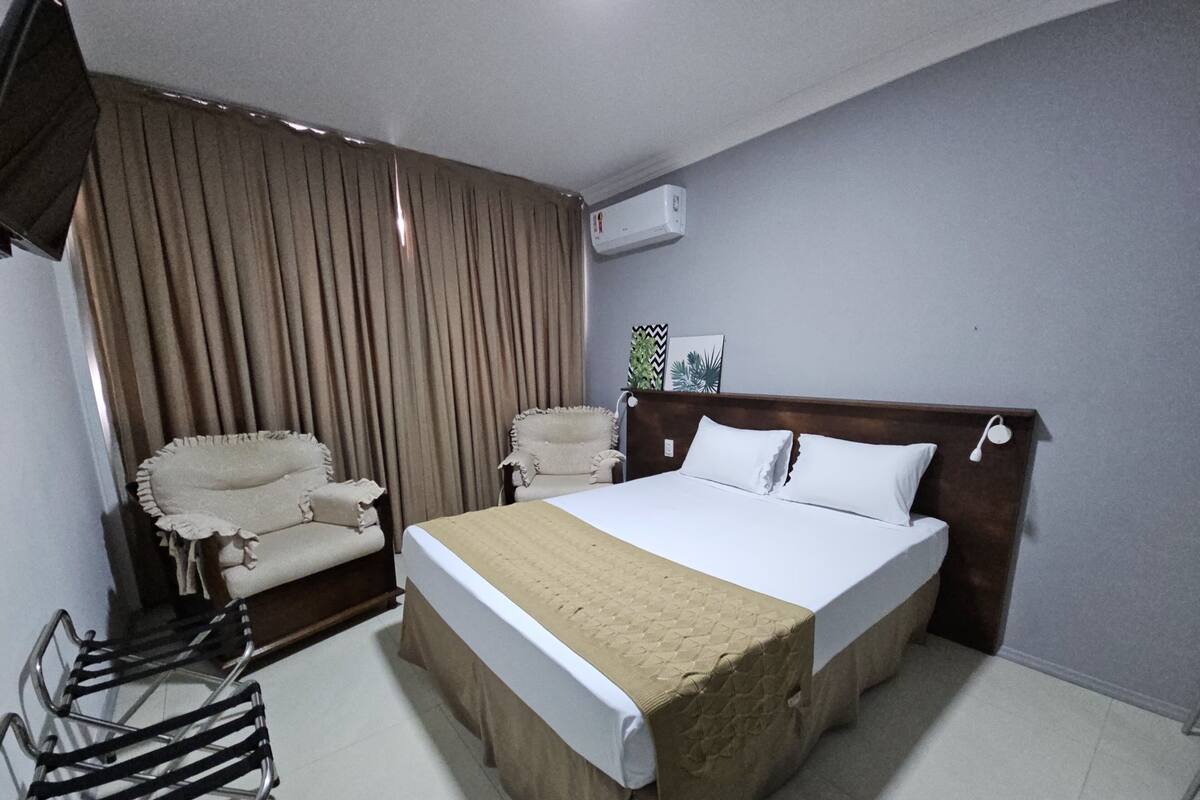 Quarto de hotel com cama, cadeira, escrivaninha e ar condicionado.