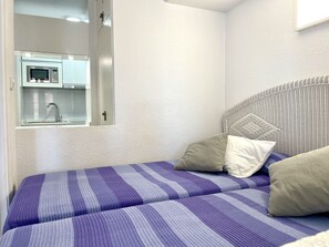 Quarto com cama, almofadas e vista para uma cozinha com micro-ondas.