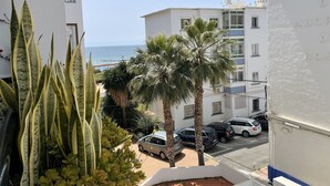 A residential building with a view of the sea, parked cars, and a palm tree.