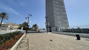 A modern high-rise building with a glass facade, a pedestrian walkway, and a water feature.