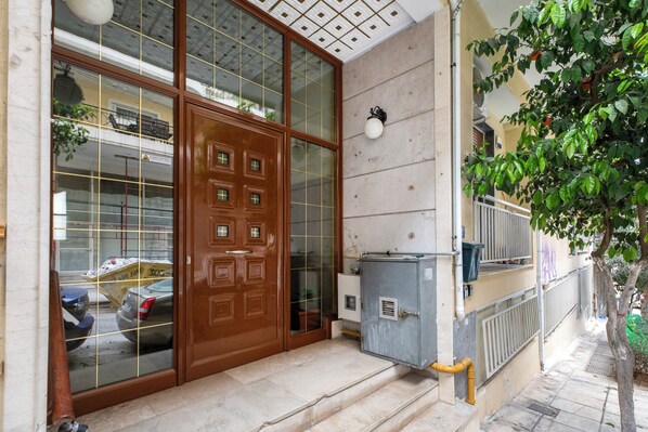 A building entrance with a wooden door, a tiled ground, and a metal fence. - Arco - 2-BR Apt in the Heart of Athens  (Athens)