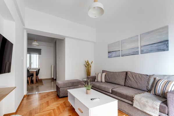 A modern living room with a sofa, a coffee table, and a dining area with chairs. - Arco - 2-BR Apt in the Heart of Athens  (Athens)