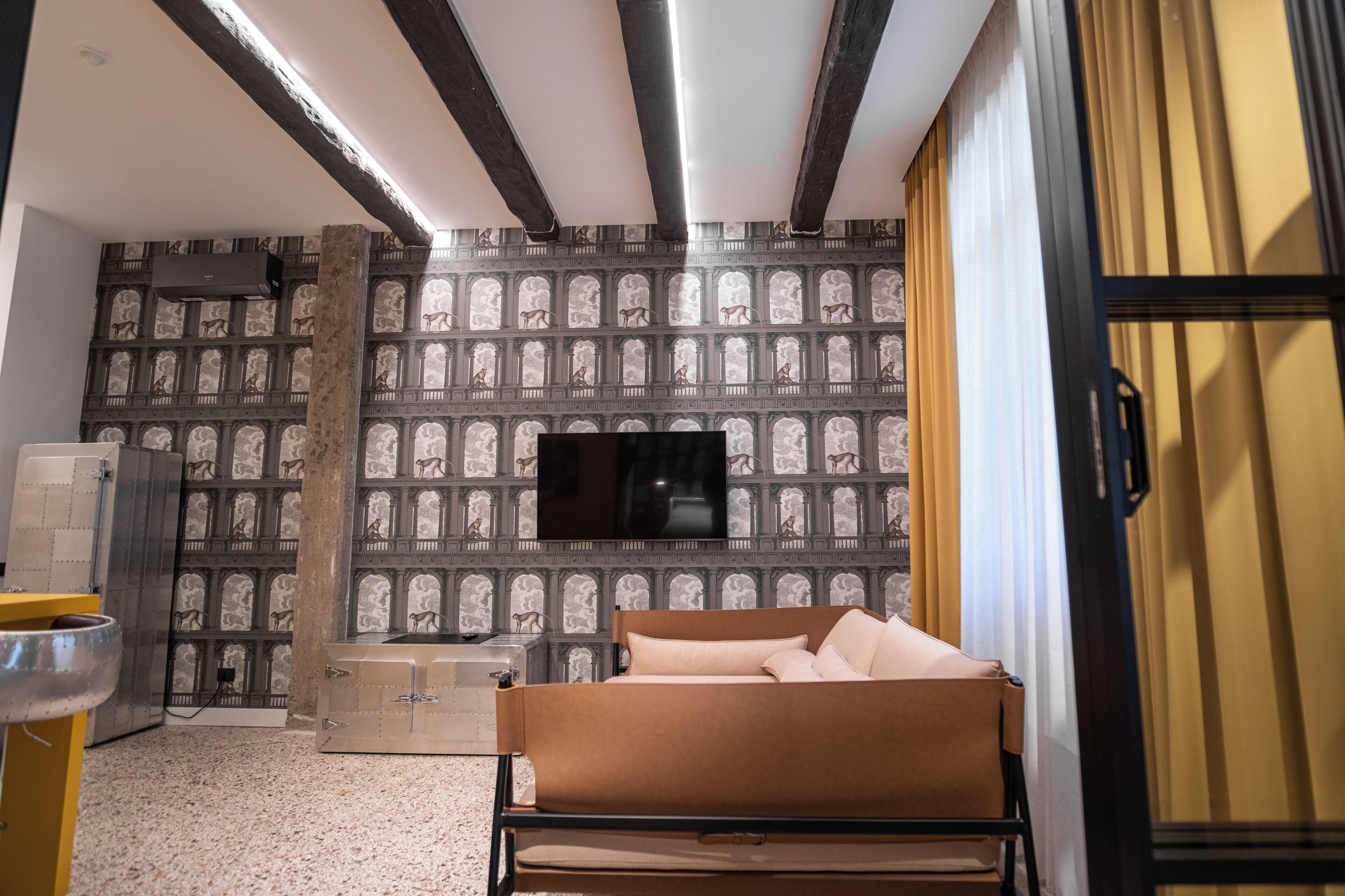 Een moderne hotelkamer met behang met een patroon, een flatscreen televisie aan de muur, een bed met hoofdeinde en een raam met gordijnen.