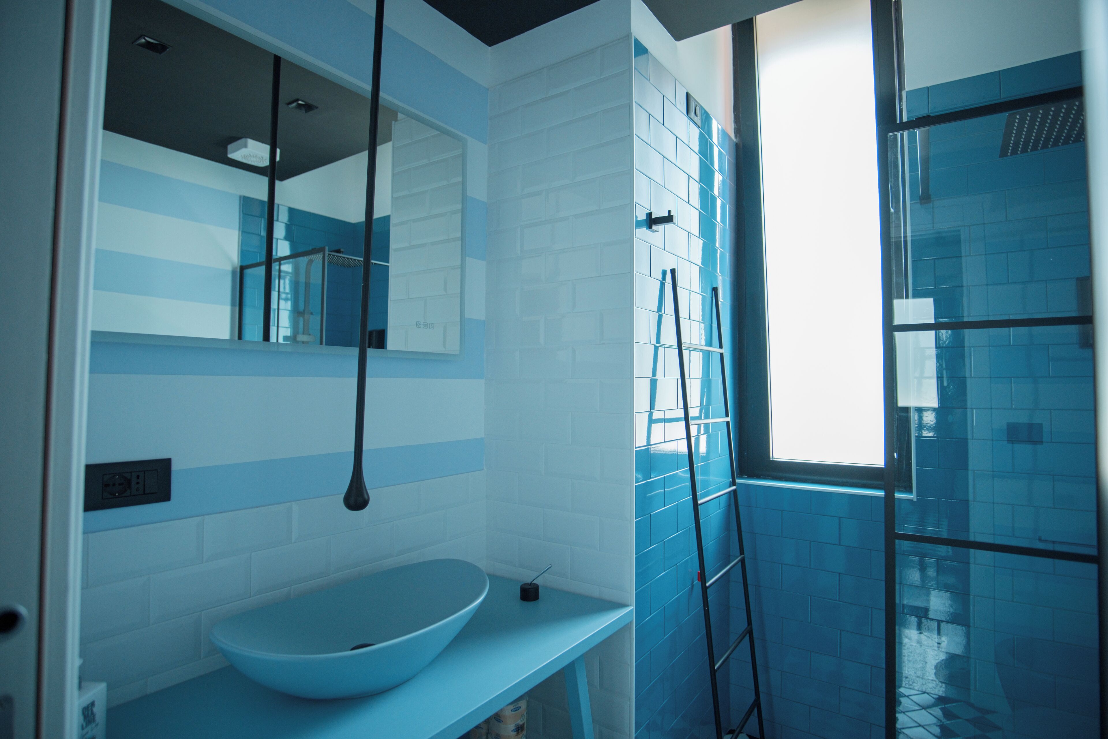 A bathroom with a blue sink, a mirror, and a shower area with blue tiles.