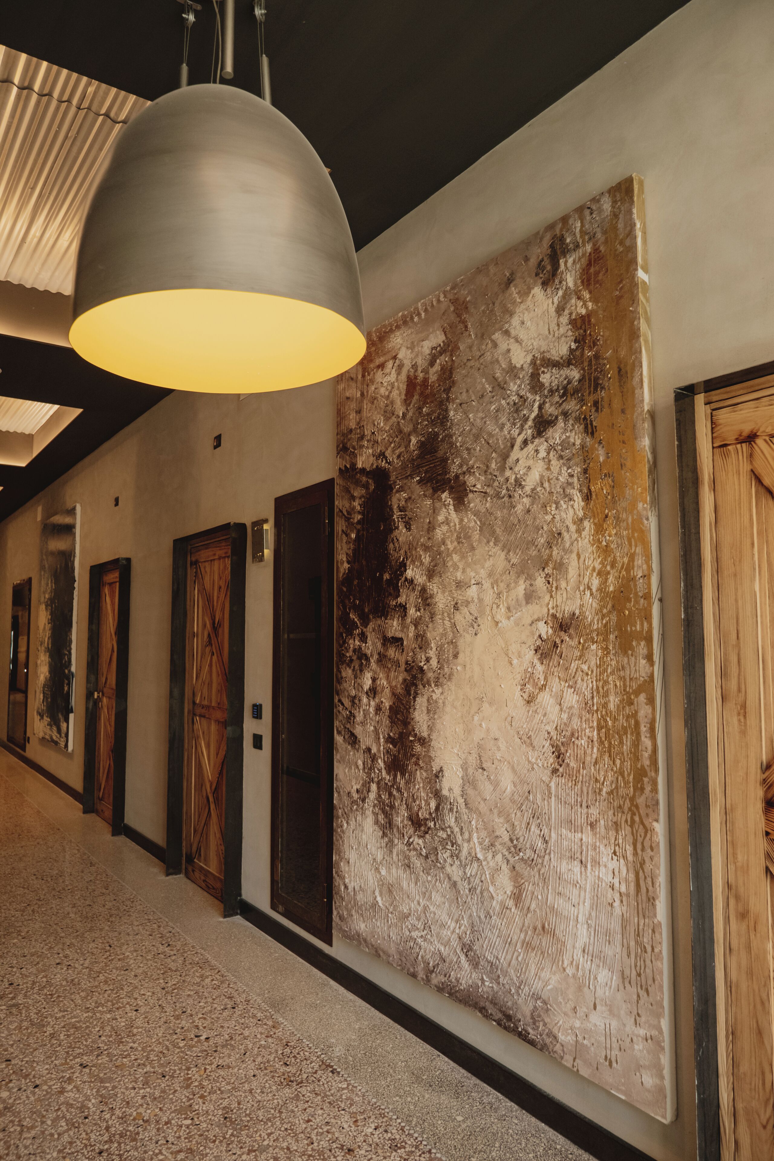 A hallway with a large textured wall, wooden doors, and a hanging light fixture.