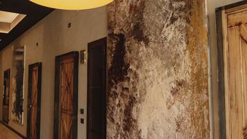 A hallway with a large textured wall, wooden doors, and a hanging light fixture.