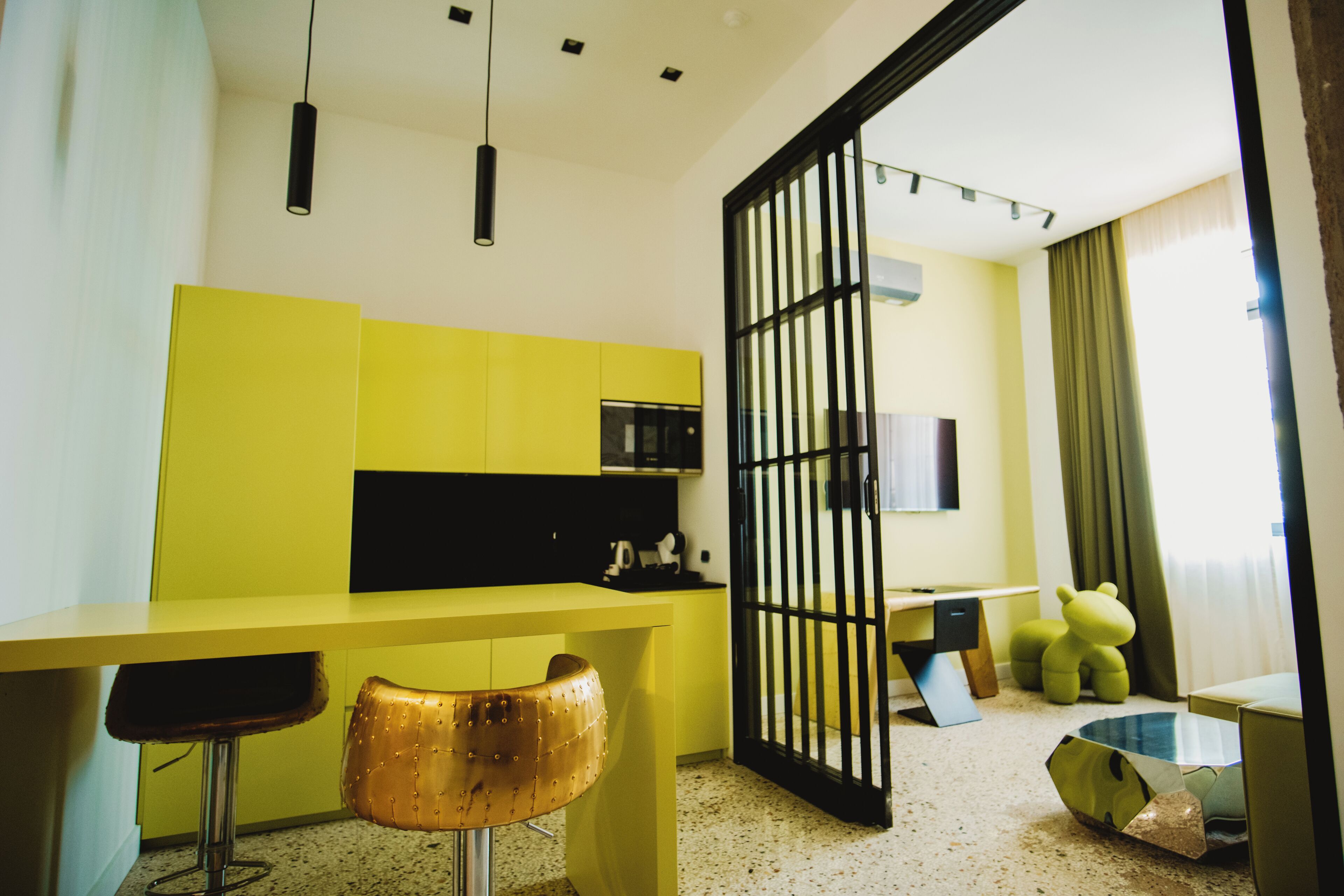 A modern kitchen with yellow cabinets, a black-framed glass door, and a bar area with stools.