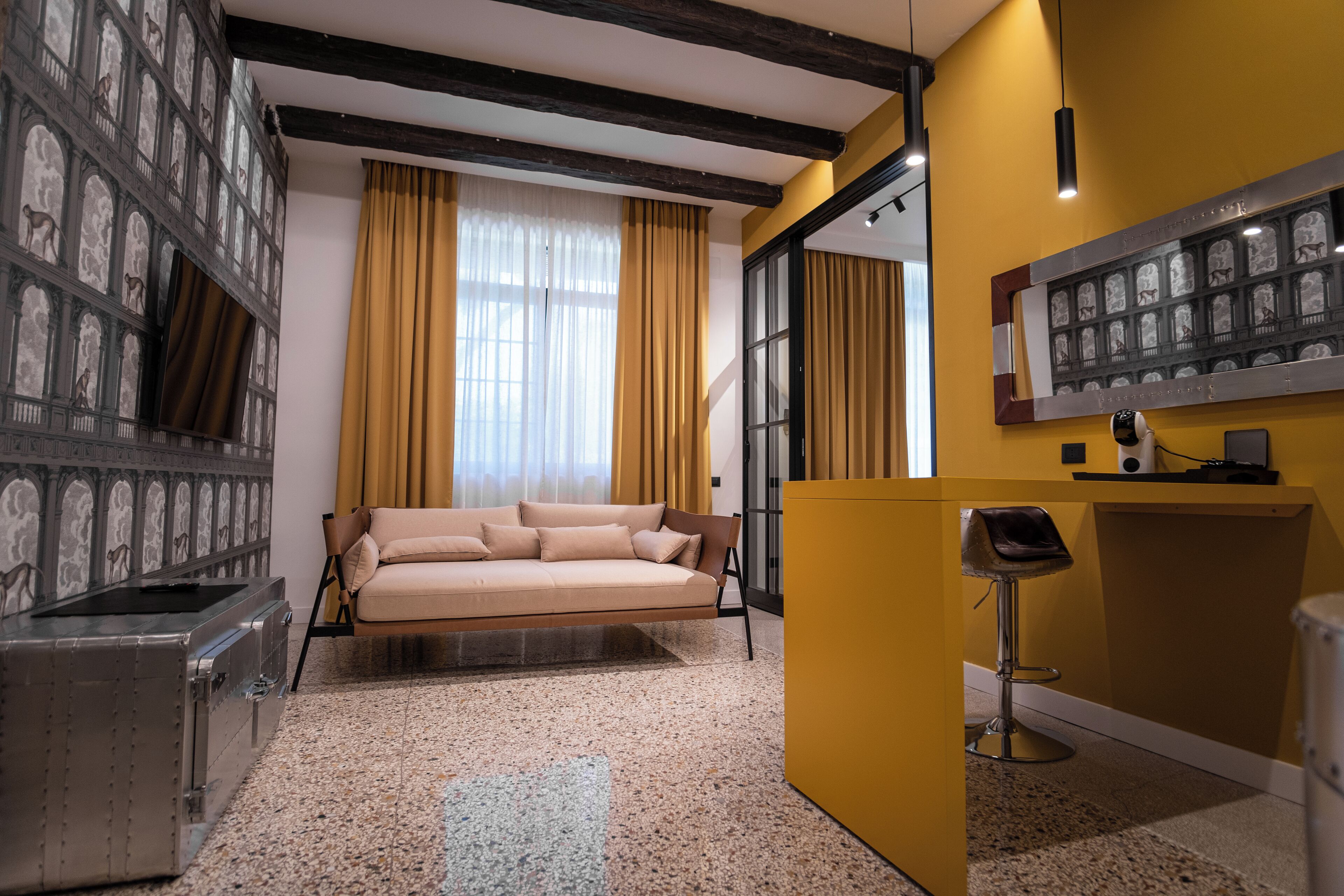 A room with a sofa, a small bar area, a large mirror, and a decorative wall with framed pictures.